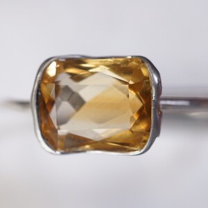 May include: A silver ring with a large, faceted, yellow topaz gemstone.