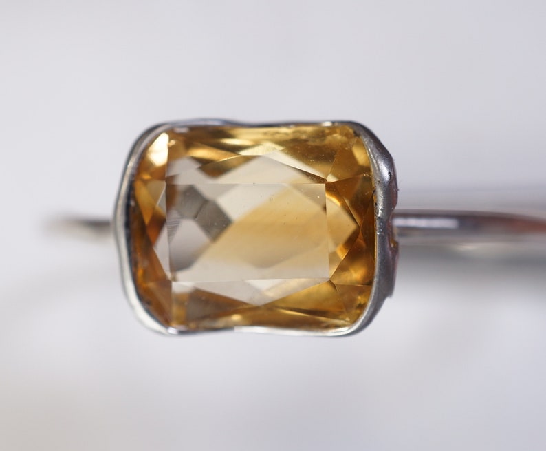 May include: A silver ring with a large, faceted, yellow topaz gemstone.