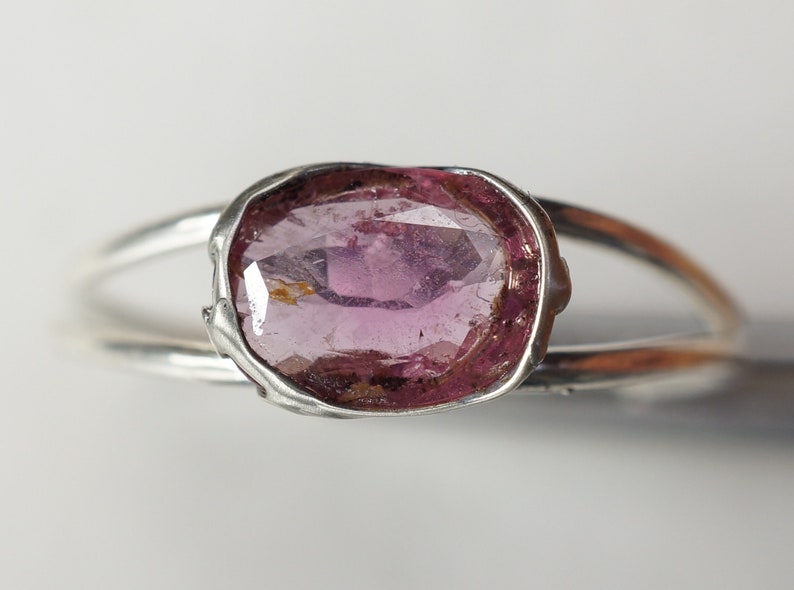 K&ouml;nnte beinhalten: Ein silberner Ring mit einem rosafarbenen ovalen Edelstein, der in einer strukturierten Silberfassung sitzt.