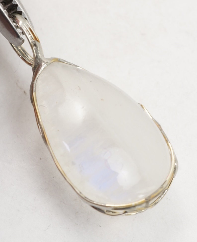 May include: A silver pendant with a teardrop-shaped moonstone set in a silver bezel. The moonstone has a milky white color with a hint of blue.