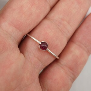 K&ouml;nnte beinhalten: Ein silberner Ring mit einem kleinen, runden, dunkelroten Edelstein.