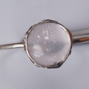 Puede incluir: Un anillo de plata con una piedra preciosa redonda, clara y rosa p&aacute;lida engastada en un delicado engaste adornado.