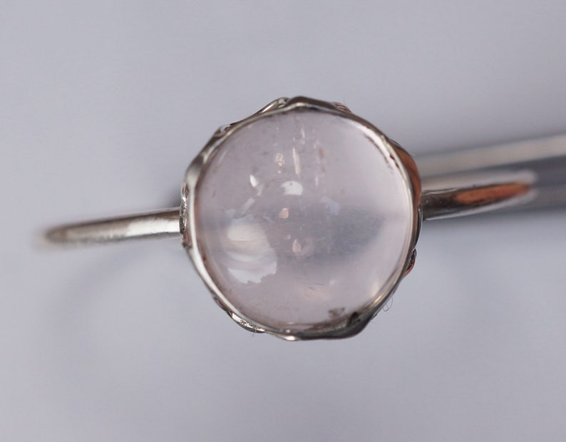 Puede incluir: Un anillo de plata con una piedra preciosa redonda, clara y rosa p&aacute;lida engastada en un delicado engaste adornado.