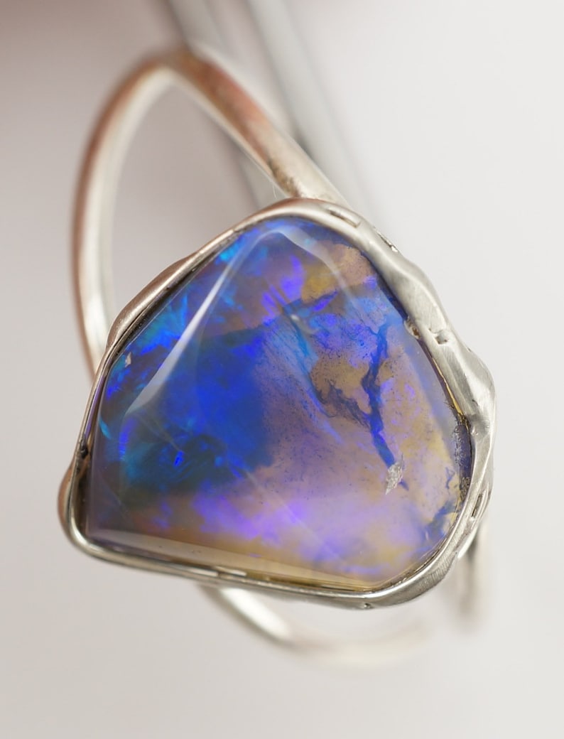 May include: A silver ring with a large, blue opal gemstone. The opal has a unique, iridescent pattern.