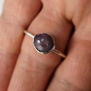 May include: A silver ring with a purple gemstone set in a wire-wrapped bezel.