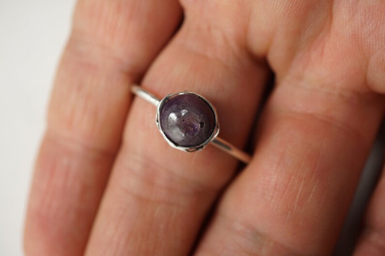May include: A silver ring with a purple gemstone set in a wire-wrapped bezel.