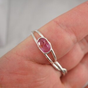 Puede incluir: Un anillo de plata con una piedra ovalada rosa engastada en el centro. El anillo est&aacute; en un dedo.