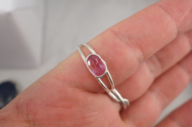 Puede incluir: Un anillo de plata con una piedra ovalada rosa engastada en el centro. El anillo est&aacute; en un dedo.