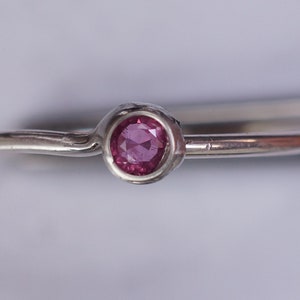 K&ouml;nnte beinhalten: Ein schlichter Silberring mit einem kleinen, runden, rosafarbenen Edelstein in der Mitte.
