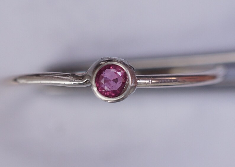 K&ouml;nnte beinhalten: Ein schlichter Silberring mit einem kleinen, runden, rosafarbenen Edelstein in der Mitte.