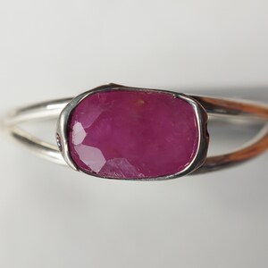 May include: A silver ring with a large, faceted, pink ruby gemstone set in a bezel setting.