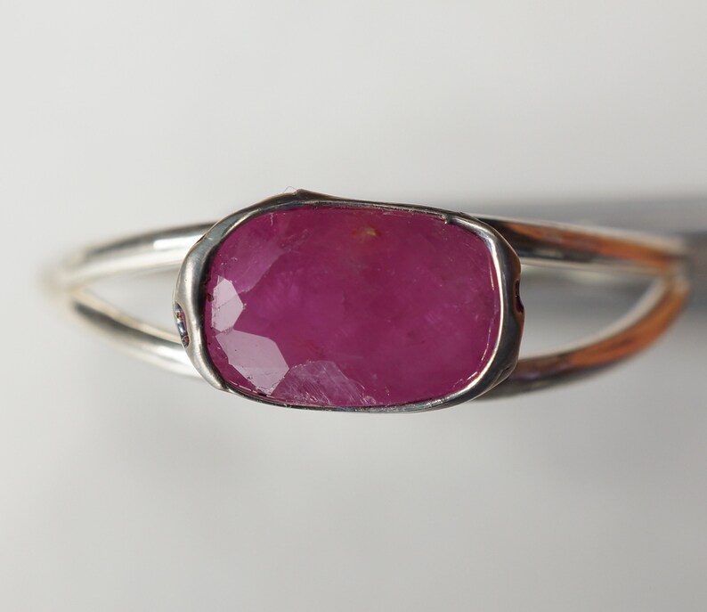 May include: A silver ring with a large, faceted, pink ruby gemstone set in a bezel setting.