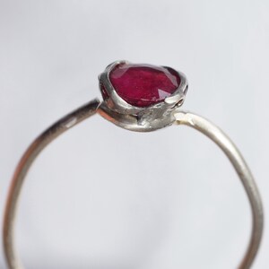 Pode incluir: Um anel de prata com uma gema vermelha engastada em uma configura&ccedil;&atilde;o texturizada de forma org&acirc;nica.