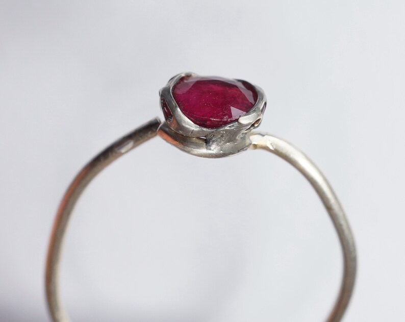 Pode incluir: Um anel de prata com uma gema vermelha engastada em uma configura&ccedil;&atilde;o texturizada de forma org&acirc;nica.