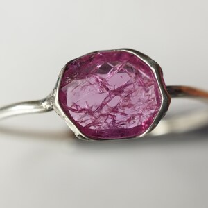 May include: A silver ring with a large, faceted, pink gemstone. The gemstone has a unique, natural, crystalline structure.