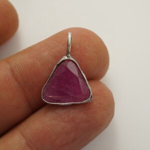 May include: A triangular pendant featuring a pink ruby gemstone set in silver.