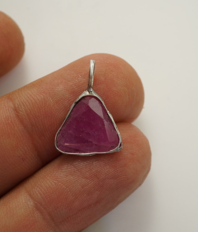 May include: A triangular pendant featuring a pink ruby gemstone set in silver.