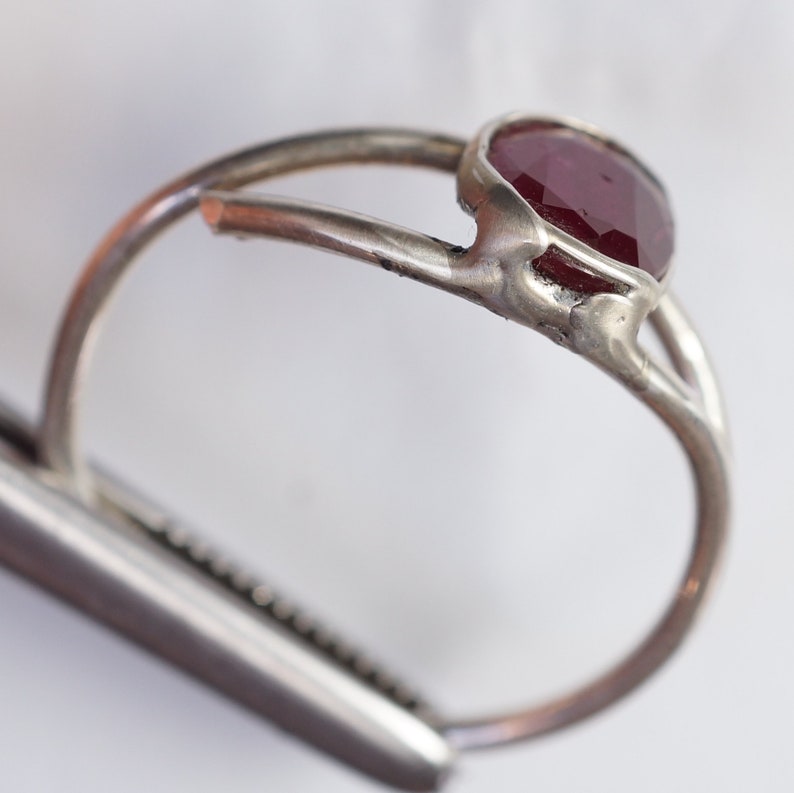 K&ouml;nnte beinhalten: Ein silberner Ring mit einem roten Edelstein, der in einer Zargenfassung sitzt. Der Ring ist handgefertigt und hat ein rustikales, organisches Aussehen.