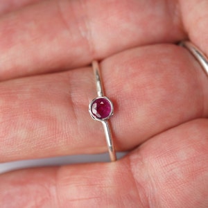 May include: A silver ring with a small, round, pink gemstone set in the center.
