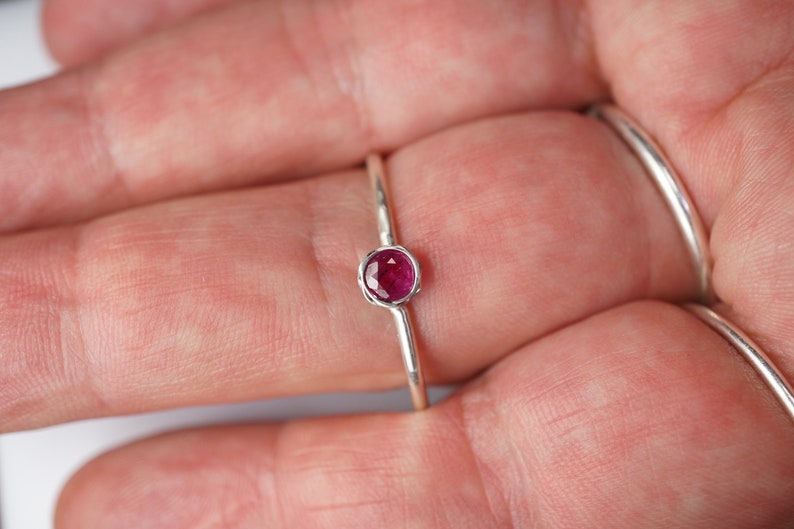 May include: A silver ring with a small, round, pink gemstone set in the center.