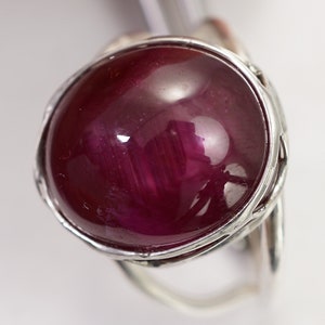 May include: A silver ring featuring a large, round, cabochon-cut ruby gemstone. The ruby is a deep red colour and has a high polish.