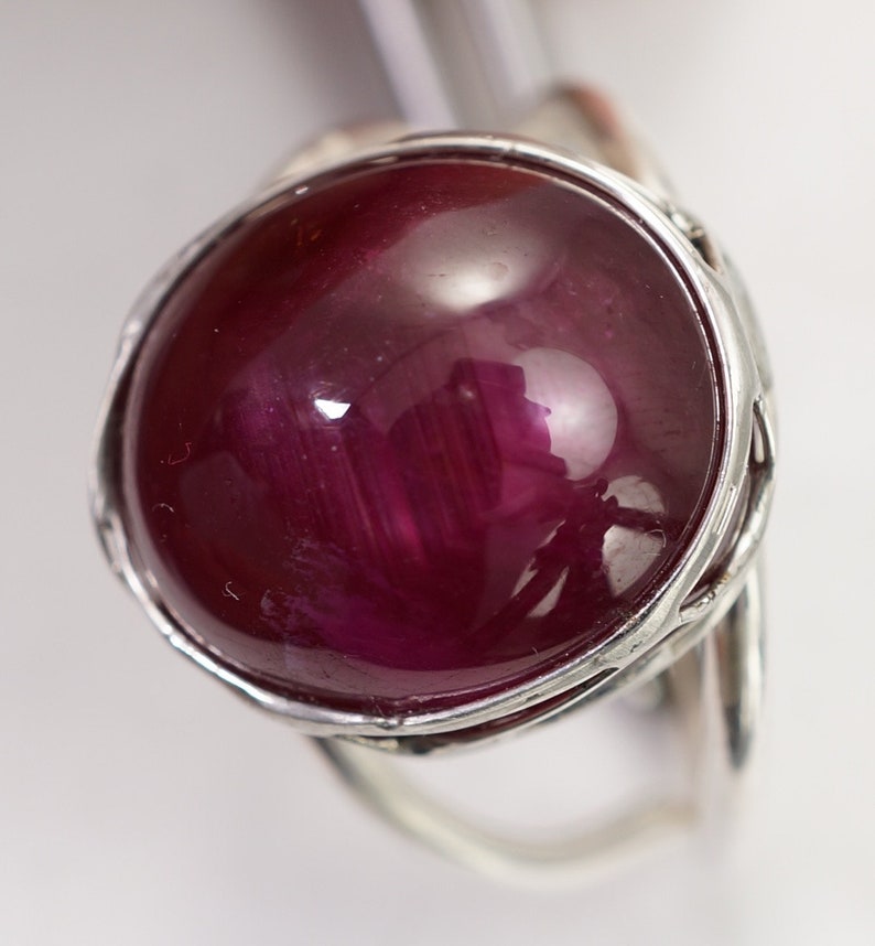 May include: A silver ring featuring a large, round, cabochon-cut ruby gemstone. The ruby is a deep red colour and has a high polish.