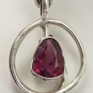 May include: A silver pendant featuring a pink gemstone set within a circular frame.