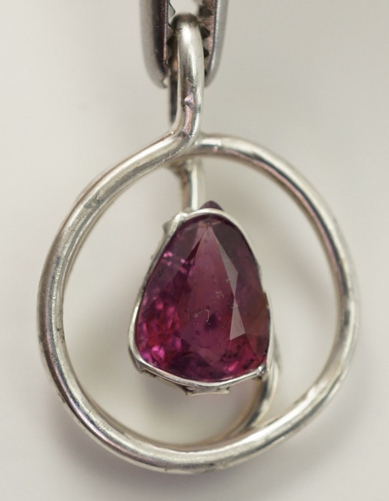 May include: A silver pendant featuring a pink gemstone set within a circular frame.