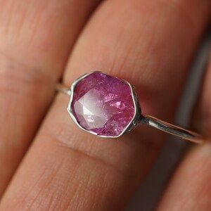 May include: A silver ring with a pink gemstone set in a faceted, irregular shape.