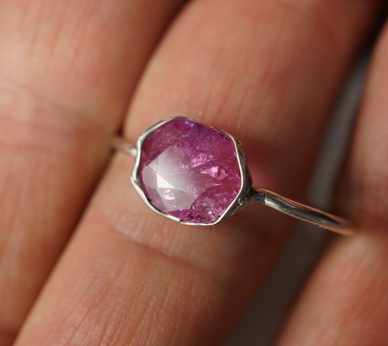 May include: A silver ring with a pink gemstone set in a faceted, irregular shape.