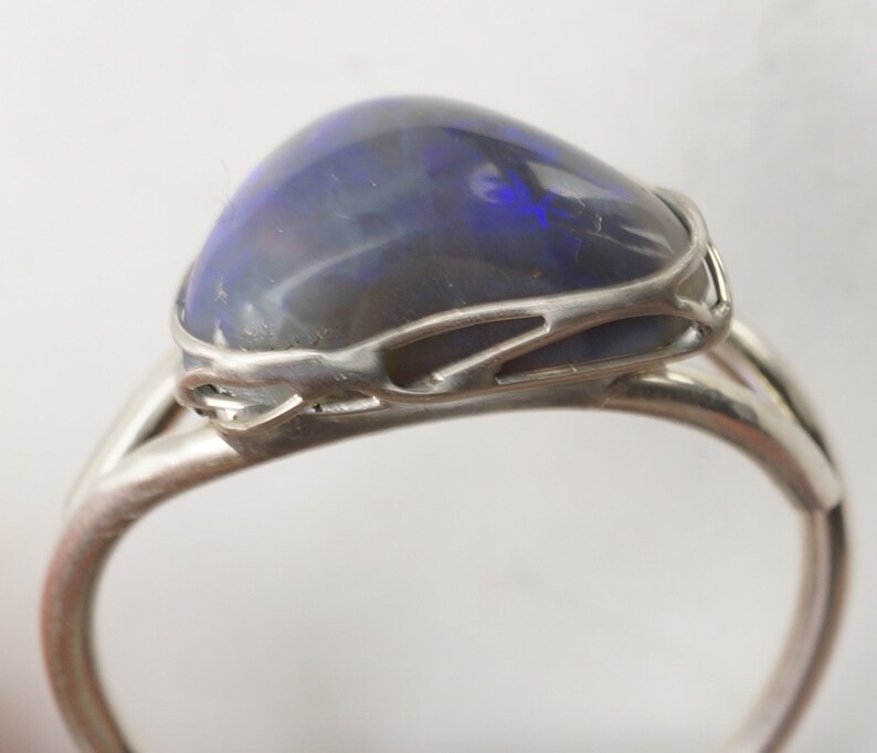 Puede incluir: Un anillo de plata con una piedra de &oacute;palo azul oscuro engastada en un dise&ntilde;o delicado e intrincado.