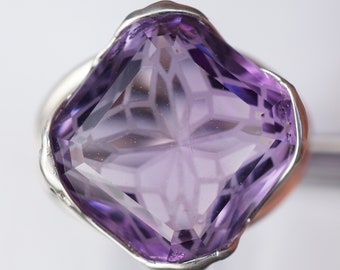 May include: A silver ring with a large, faceted amethyst gemstone. The gemstone is a deep purple color and has a geometric cut.