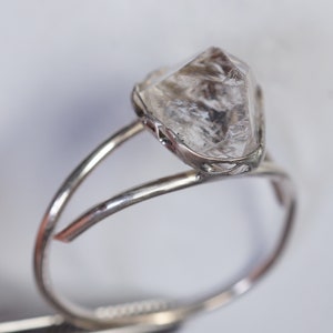 May include: A silver ring with a clear, faceted, diamond-shaped stone set in a delicate, openwork design.