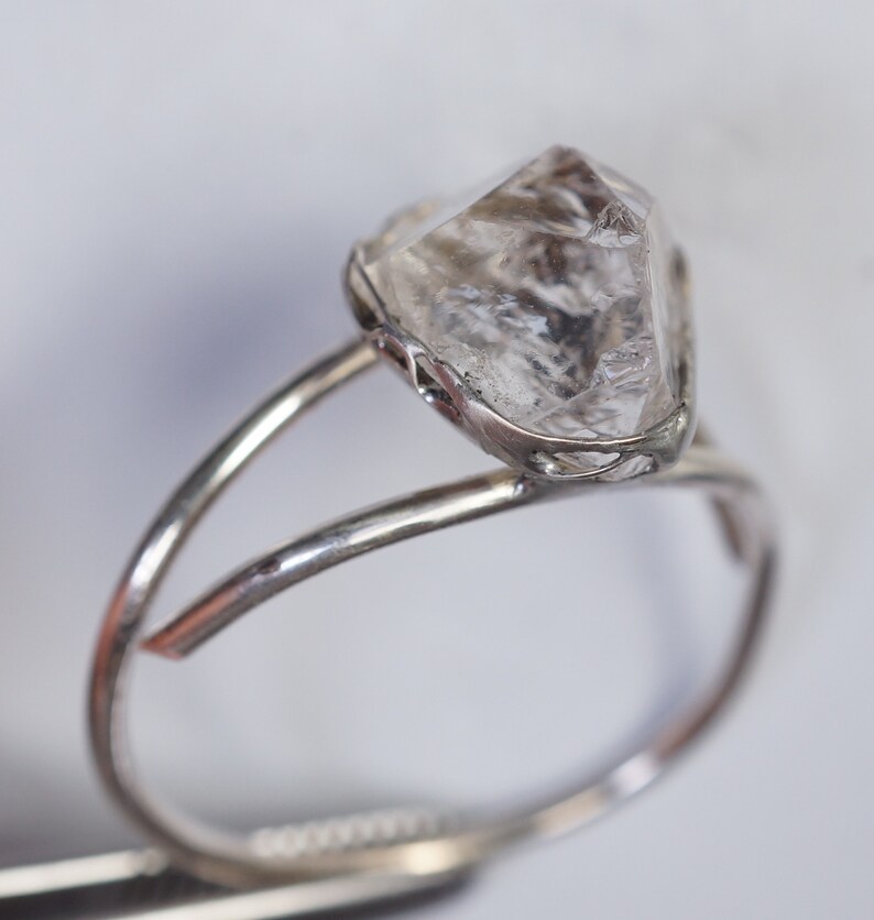 May include: A silver ring with a clear, faceted, diamond-shaped stone set in a delicate, openwork design.