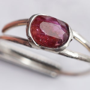 Puede incluir: Un anillo de plata con una piedra preciosa rosa engastada en un engaste de bisel. El anillo tiene una textura martillada.