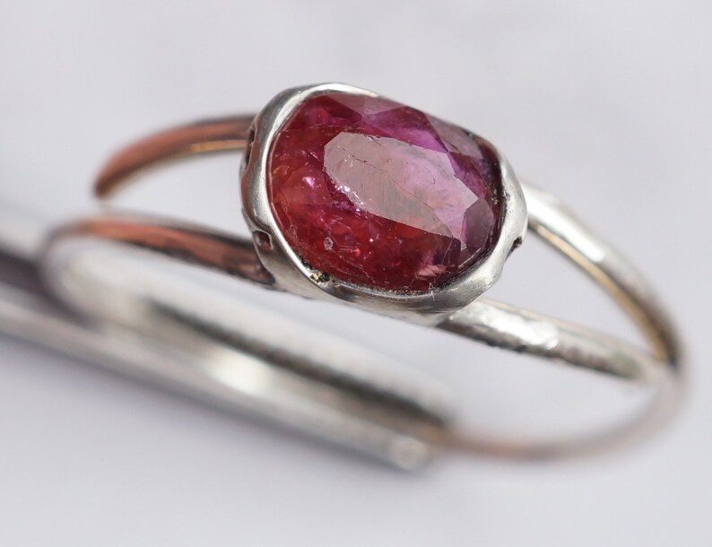 Puede incluir: Un anillo de plata con una piedra preciosa rosa engastada en un engaste de bisel. El anillo tiene una textura martillada.