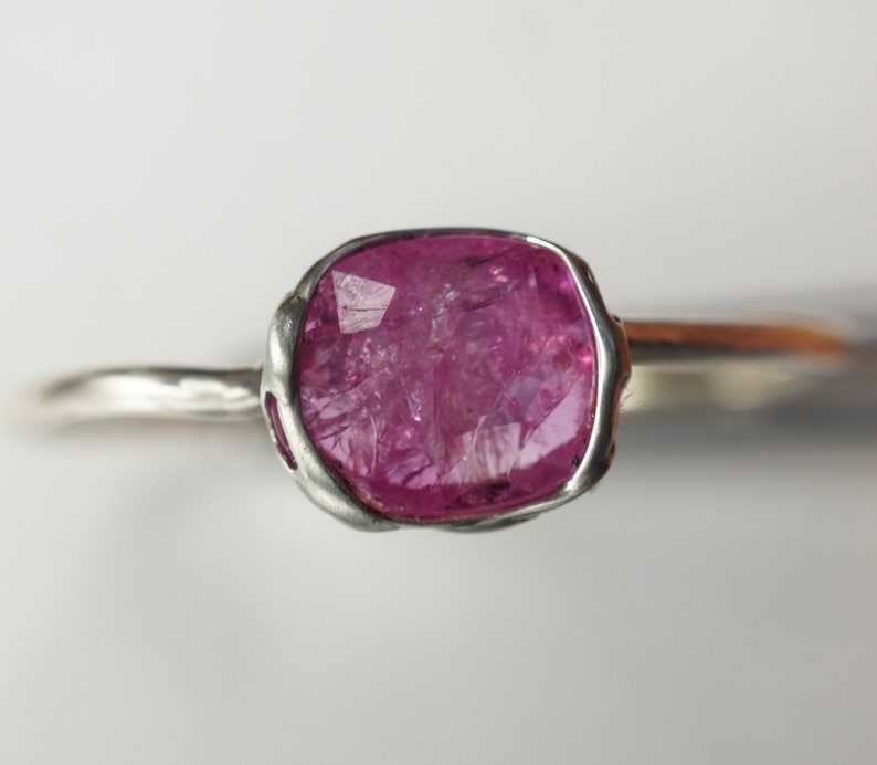 Op de afbeelding: Een zilveren ring met een roze edelsteen gezet in een getextureerde zetting. De edelsteen is ruw geslepen en heeft een natuurlijke, organische uitstraling.