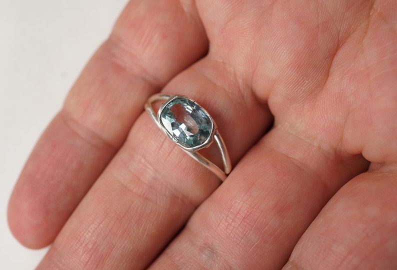 May include: A silver ring with a light blue oval gemstone.