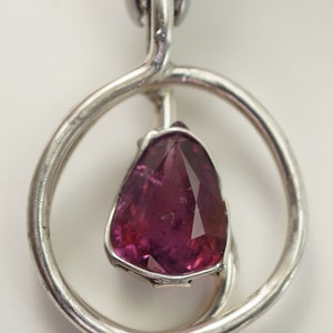 May include: A silver pendant featuring a pink gemstone set within a circular design.