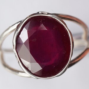 May include: A silver ring with a large, faceted ruby gemstone. The ruby is a deep red color and has a slightly oval shape.
