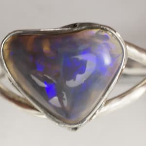 Puede incluir: Un anillo de plata con una piedra preciosa de &oacute;palo en forma de coraz&oacute;n. El &oacute;palo es de color gris oscuro con destellos de azul y morado.