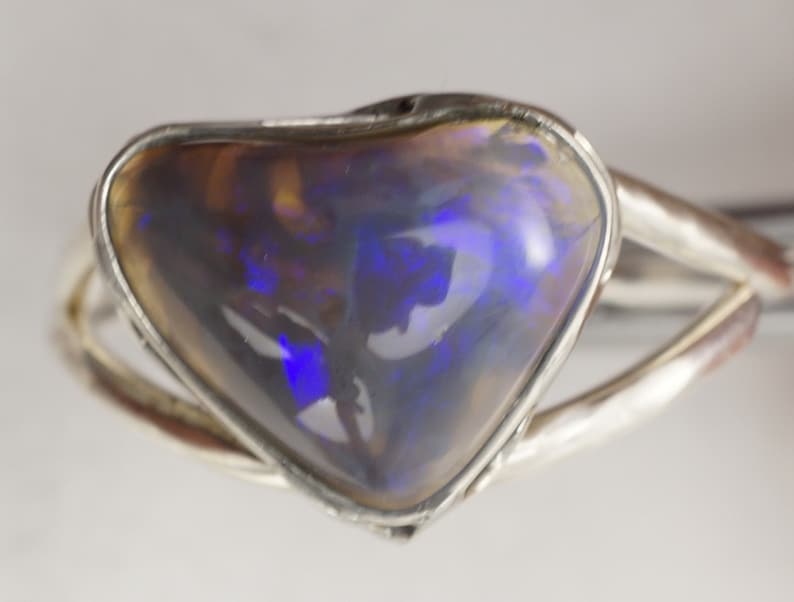 Puede incluir: Un anillo de plata con una piedra preciosa de &oacute;palo en forma de coraz&oacute;n. El &oacute;palo es de color gris oscuro con destellos de azul y morado.