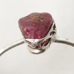 May include: A silver ring with a raw ruby gemstone set in a delicate, openwork design.