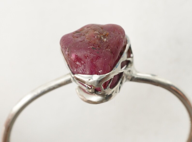May include: A silver ring with a raw ruby gemstone set in a delicate, openwork design.