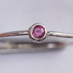 K&ouml;nnte beinhalten: Ein silberner Ring mit einem kleinen, runden, rosafarbenen Edelstein, der in einer Zargenfassung gefasst ist.