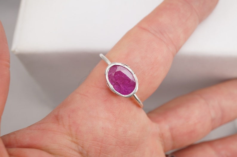 Op de afbeelding: Een zilveren ring met een roze ovale edelsteen in een bezel-setting.