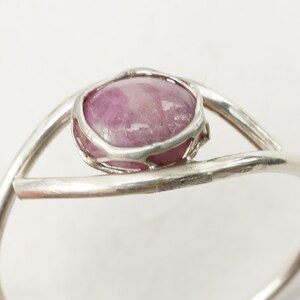 May include: A silver ring featuring a pink oval gemstone set in a delicate wire cage.