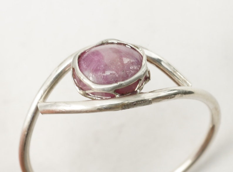 May include: A silver ring featuring a pink oval gemstone set in a delicate wire cage.