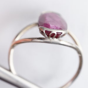 Op de afbeelding: Een zilveren ring met een grote, ovale robijn, gezet in een delicate, sierlijke zilveren zetting.