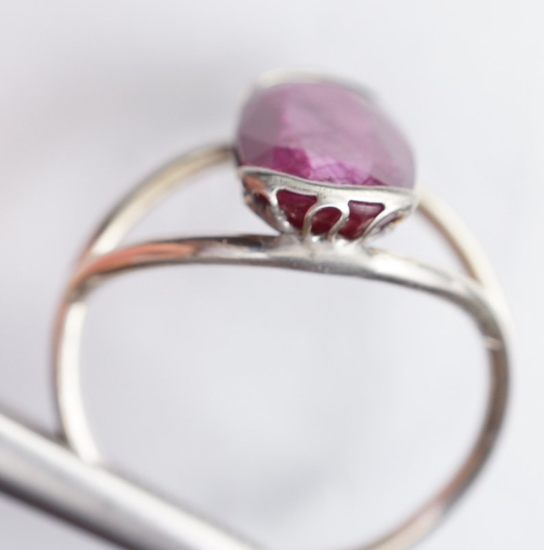 Op de afbeelding: Een zilveren ring met een grote, ovale robijn, gezet in een delicate, sierlijke zilveren zetting.